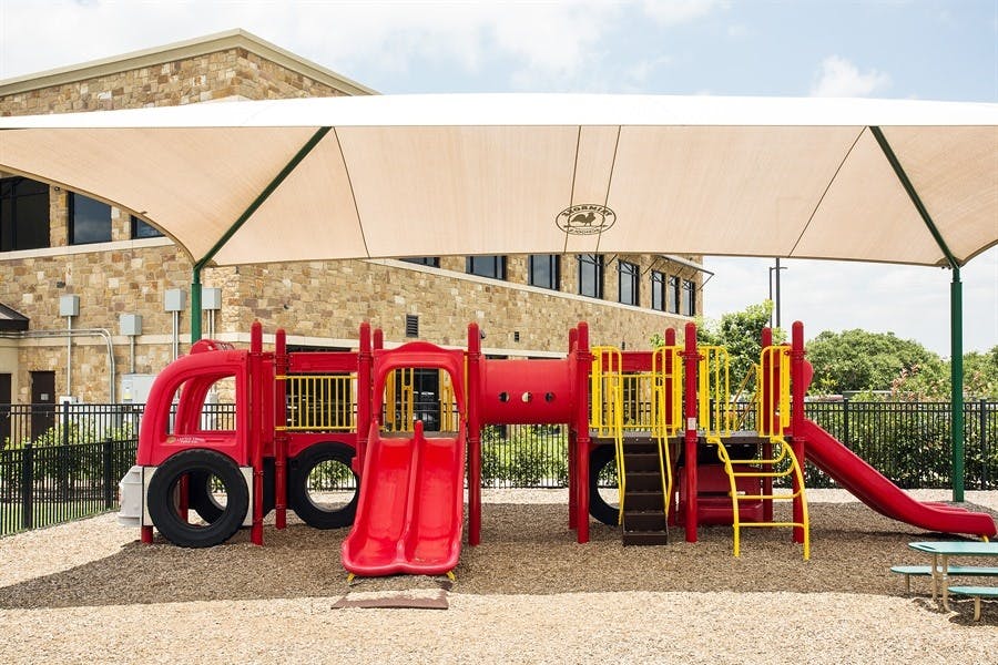 Red and yellow playground structure with slides and climbing areas under a shade sail