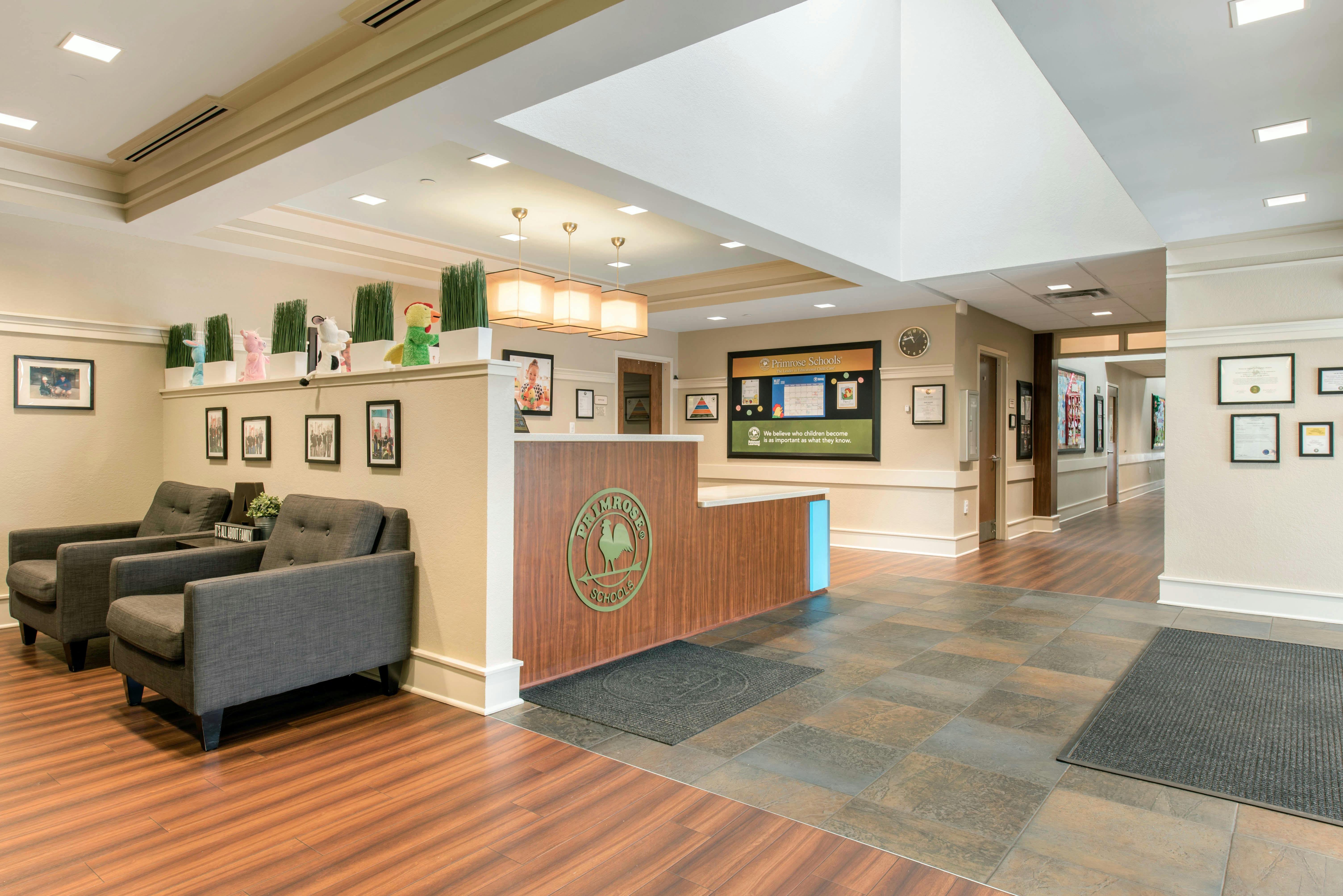 Lobby area with a reception desk featuring the Primrose Schools logo, a waiting area with two chairs, and a hallway