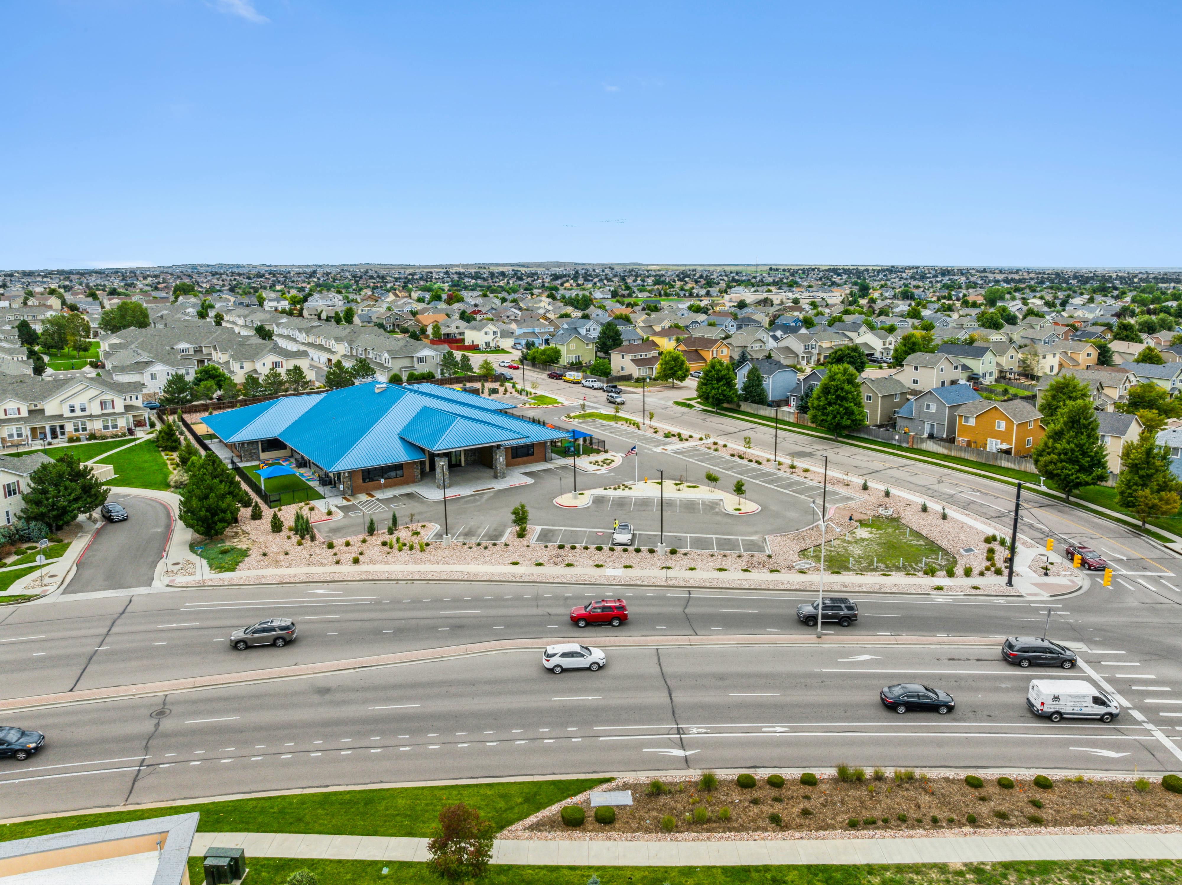 Aerial view of a suburban neighborhood with houses, a building with a blue roof, and a street with cars