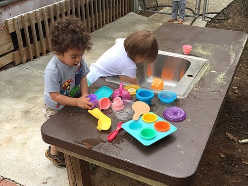 Two children playing with toys at a table with a sink