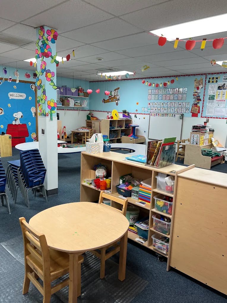 Classroom interior with small tables and wooden shelves filled with supplies