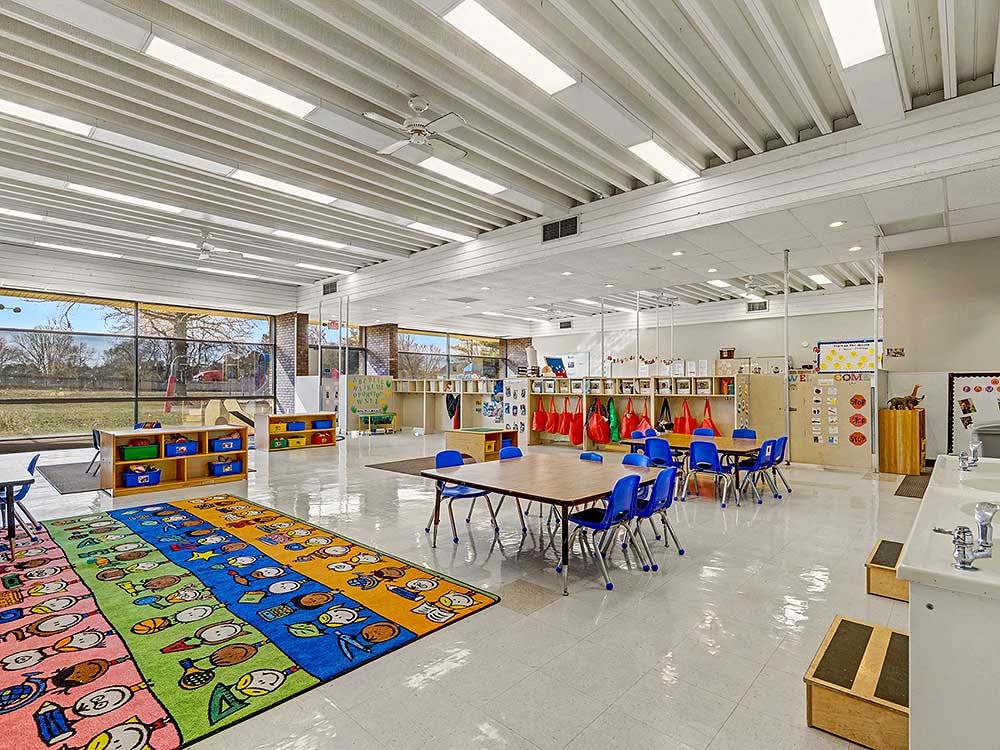 Empty colorful preschool classroom with tables, chairs, and a rug with cartoon characters