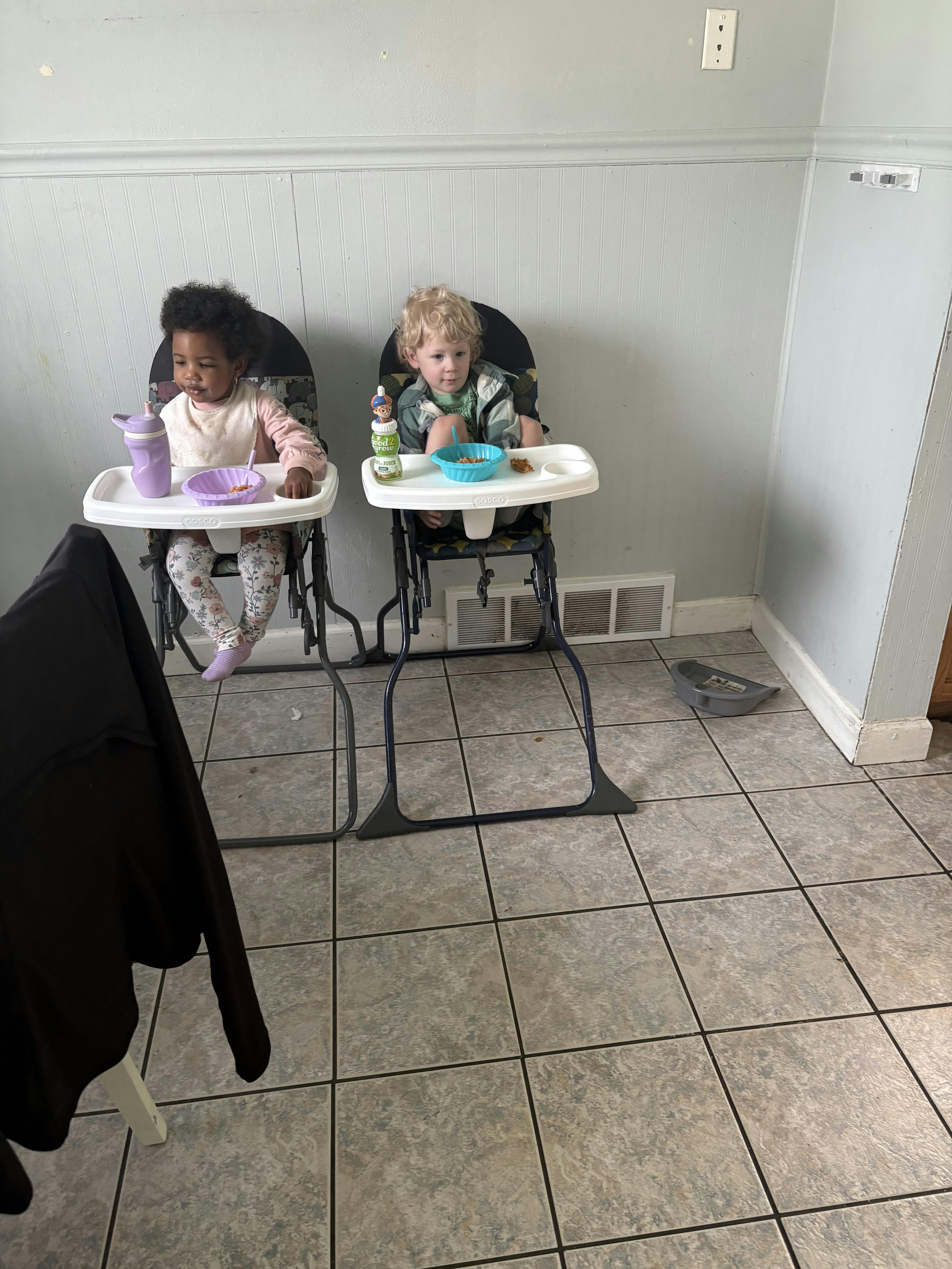 Two children sitting in high chairs with bowls of food