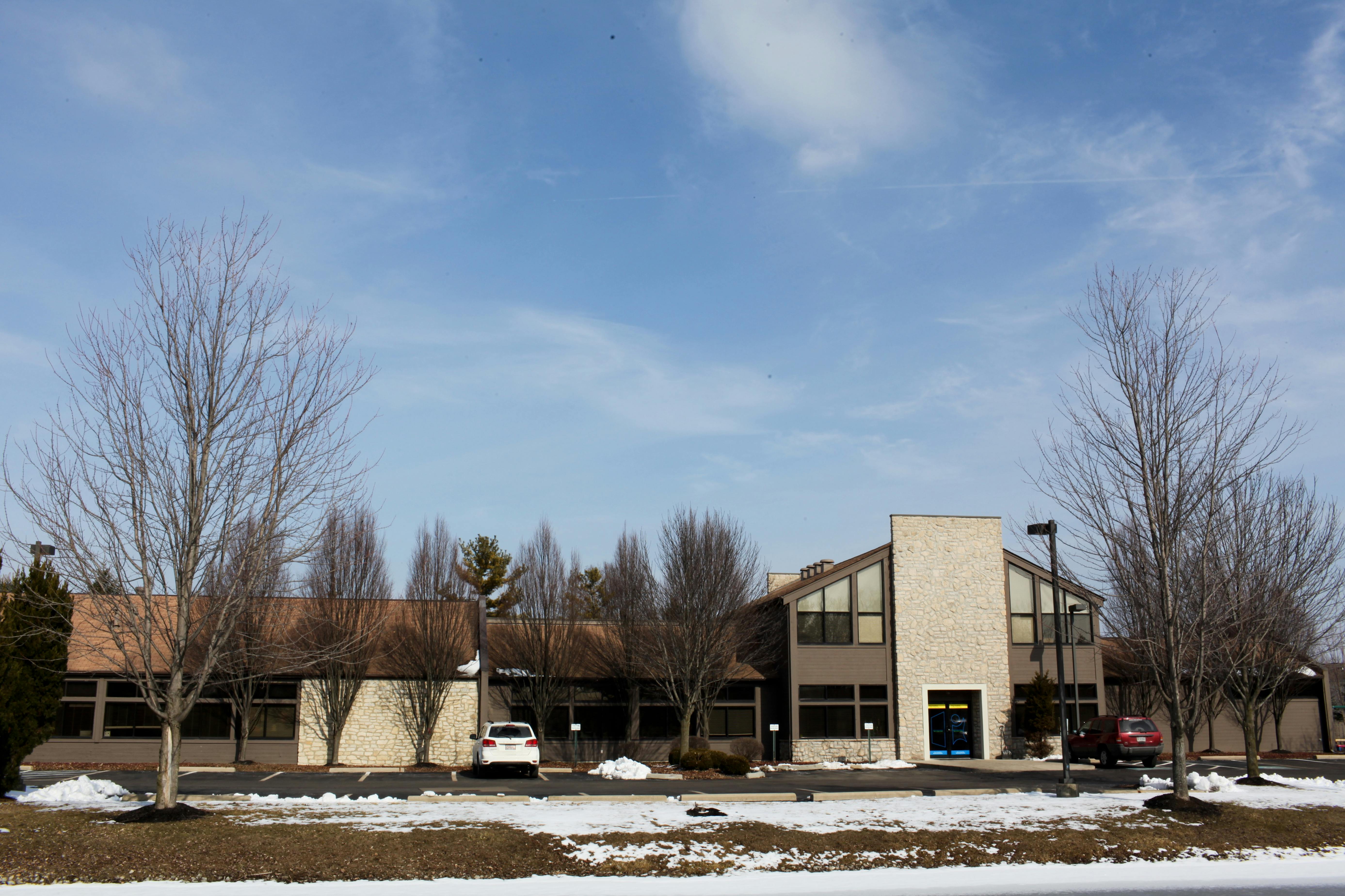 Building with a light-colored facade and dark roof, bare trees in front