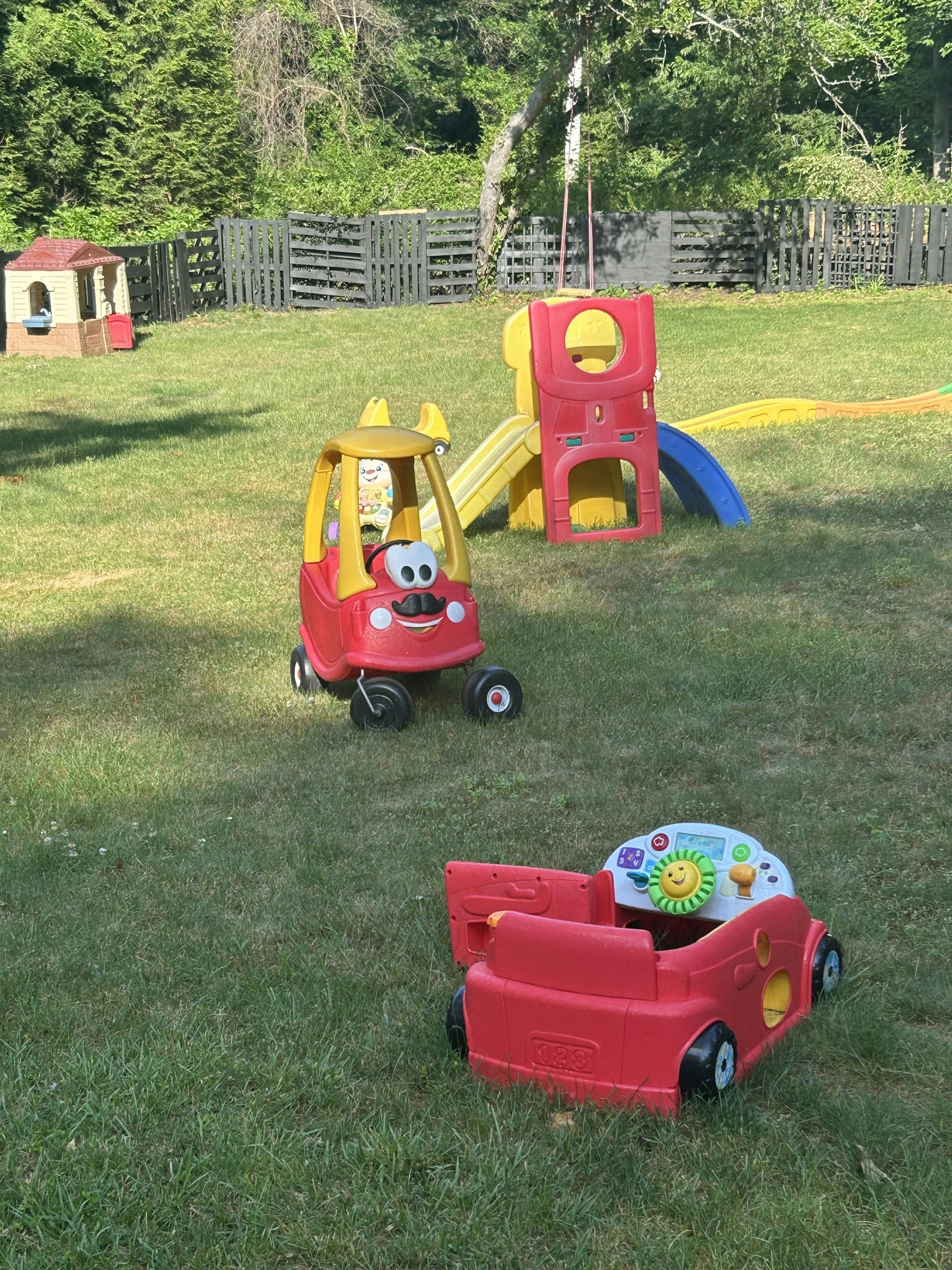 Red and yellow toy car with a mustache, a red and yellow slide, and a red toy car base in a grassy yard