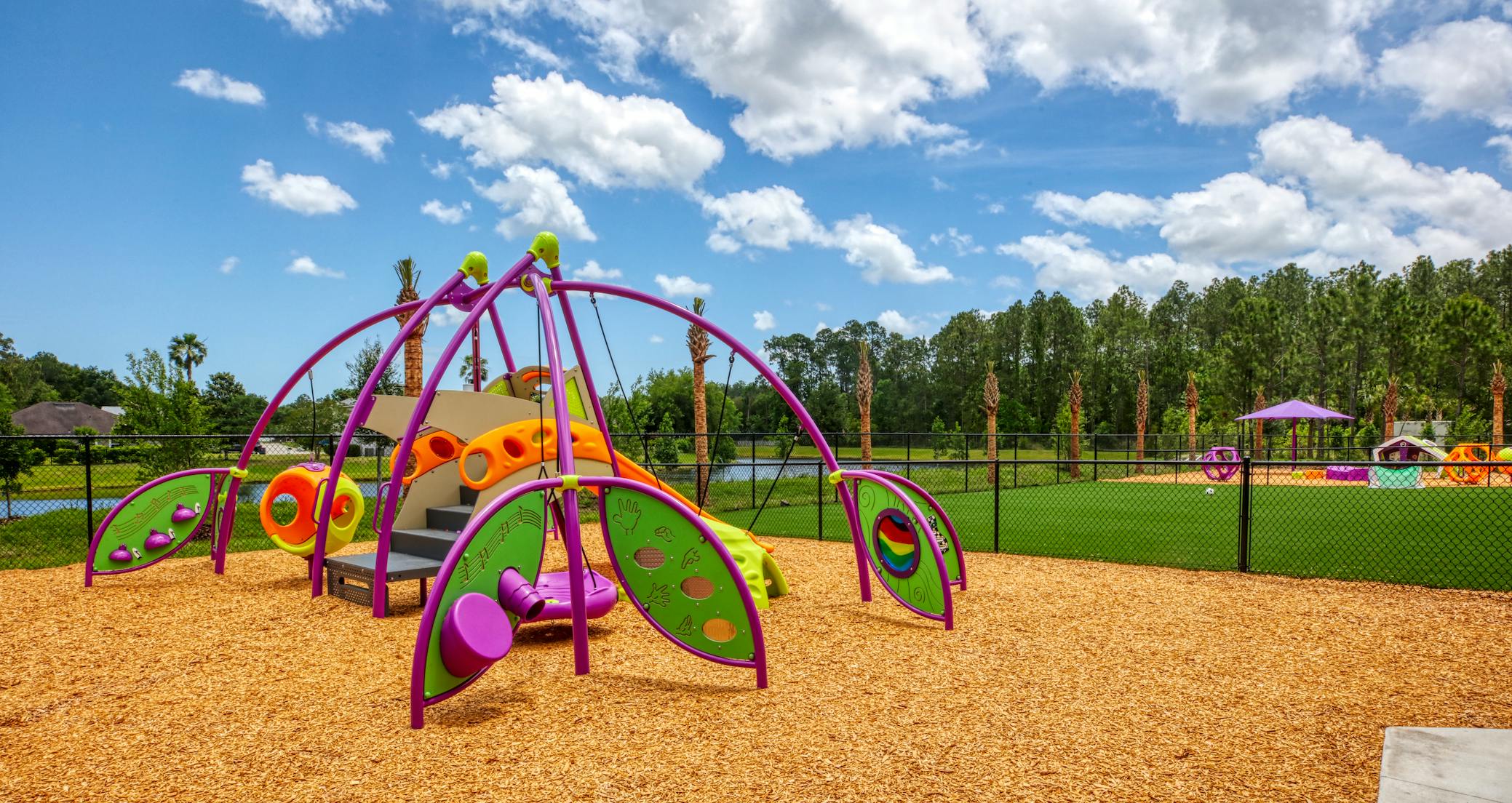 Colorful playground structure on wood chips next to a fenced turf area