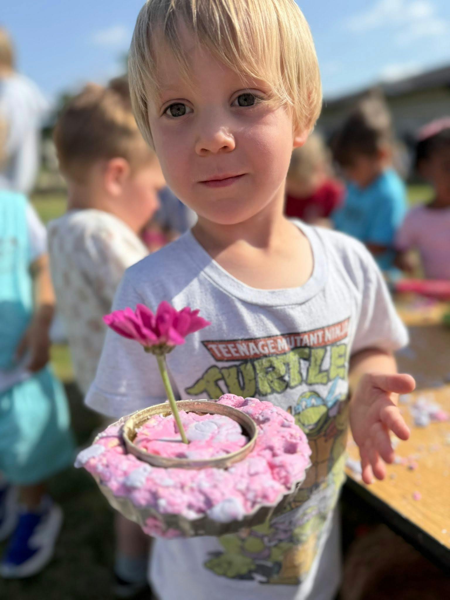 Child holding a craft made from a muffin tin, pink foam, and a flower