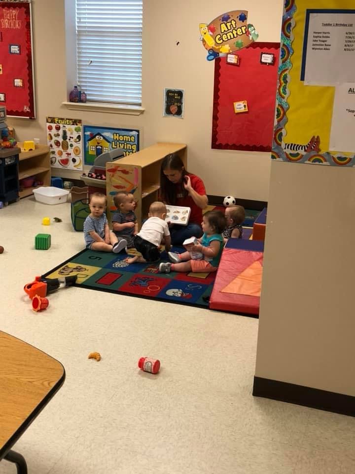 Adult reading to several children on a colorful rug in a classroom