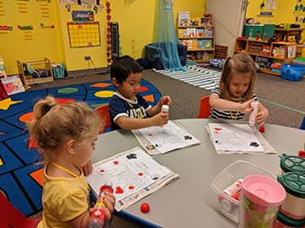 Three children doing an art activity at a table in a classroom