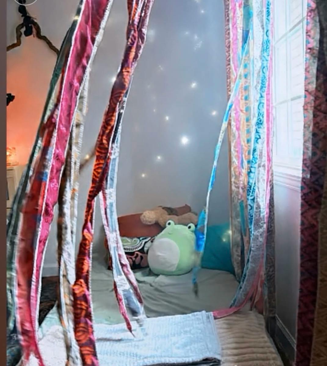 Small indoor fort draped with fabric strips containing pillows and plush toys