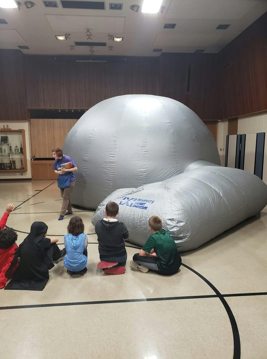 Person standing near large inflatable dome with children sitting on floor