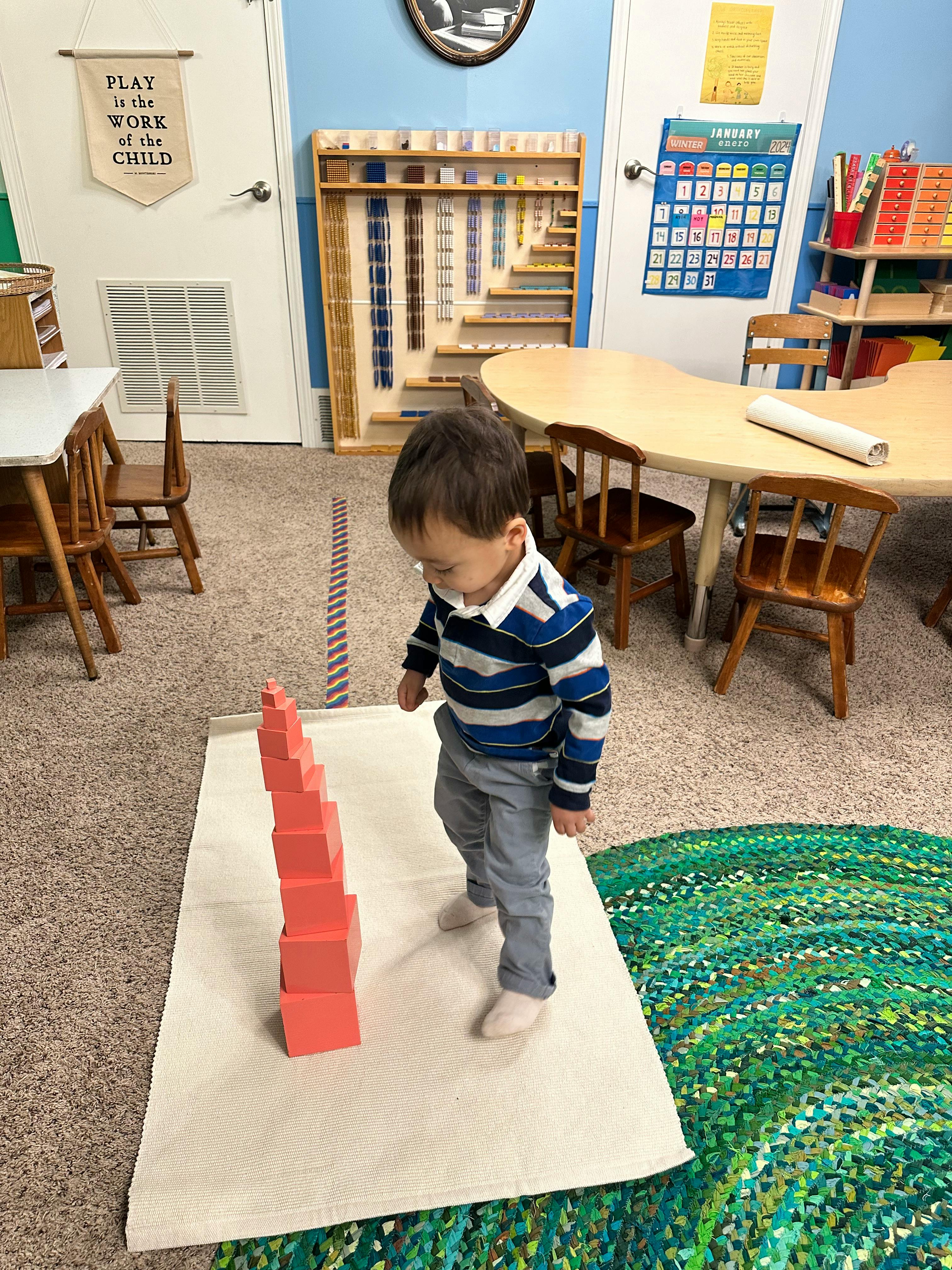 Child standing near a tower of pink blocks in a classroom