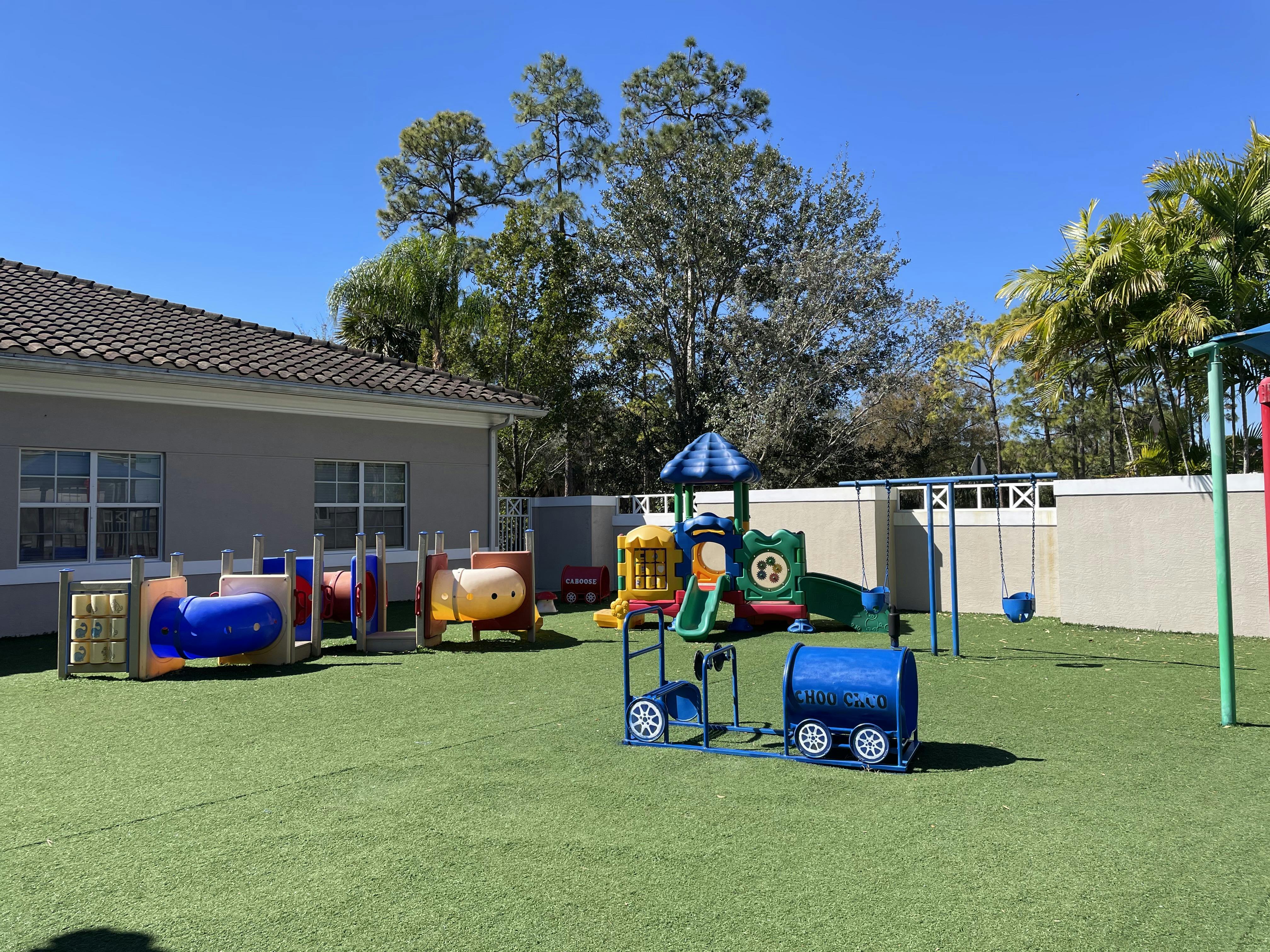 Colorful playground on artificial grass with building and trees in background