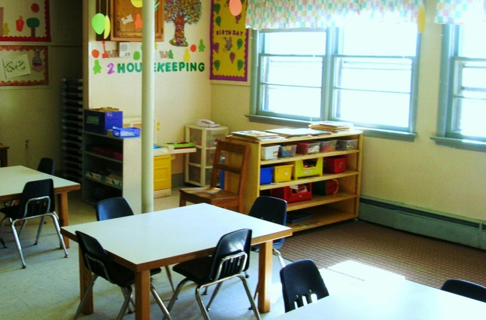 Classroom with small tables and chairs, shelves with bins, and windows