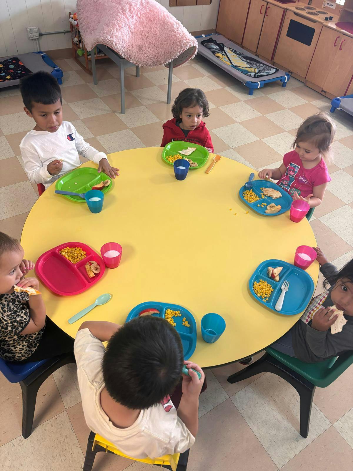 Children eating at a yellow round table in a classroom