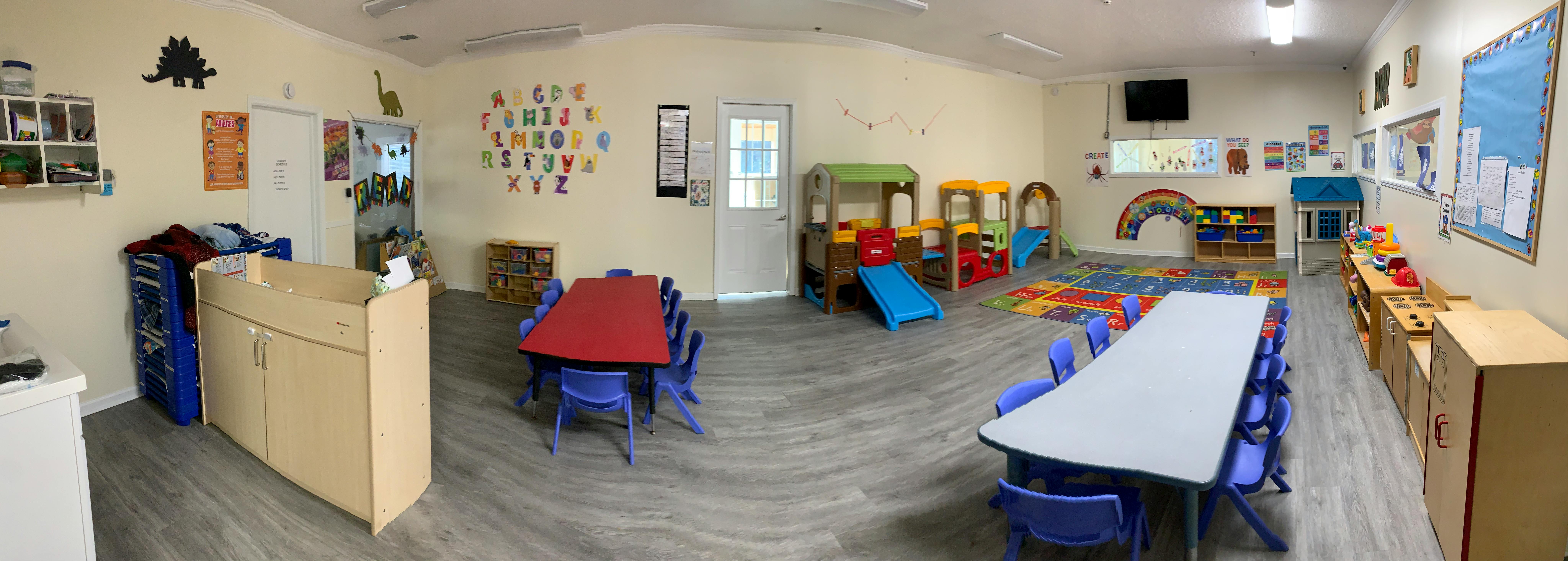 Classroom with small tables and chairs, play equipment, and wall decorations
