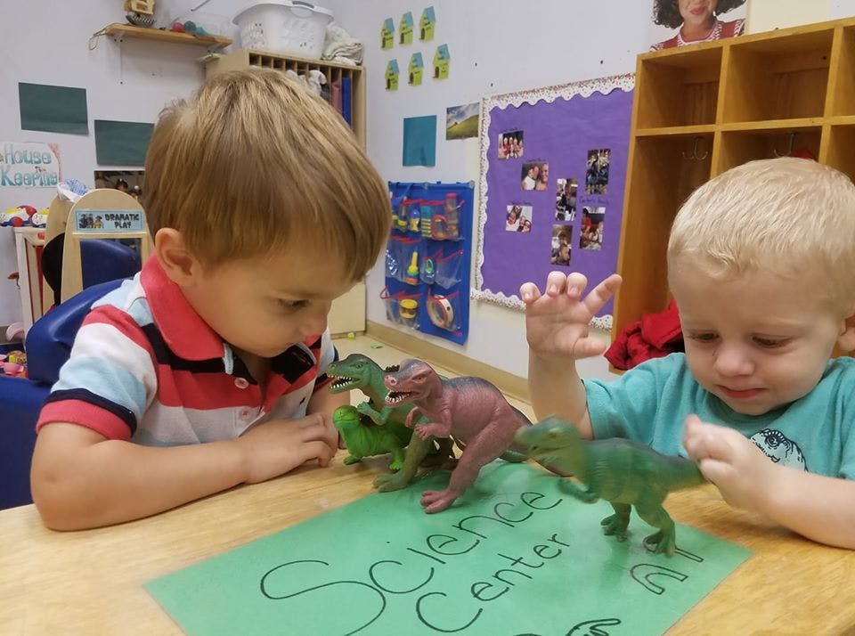 Two children playing with dinosaur toys on a table with "Science Center" written on paper