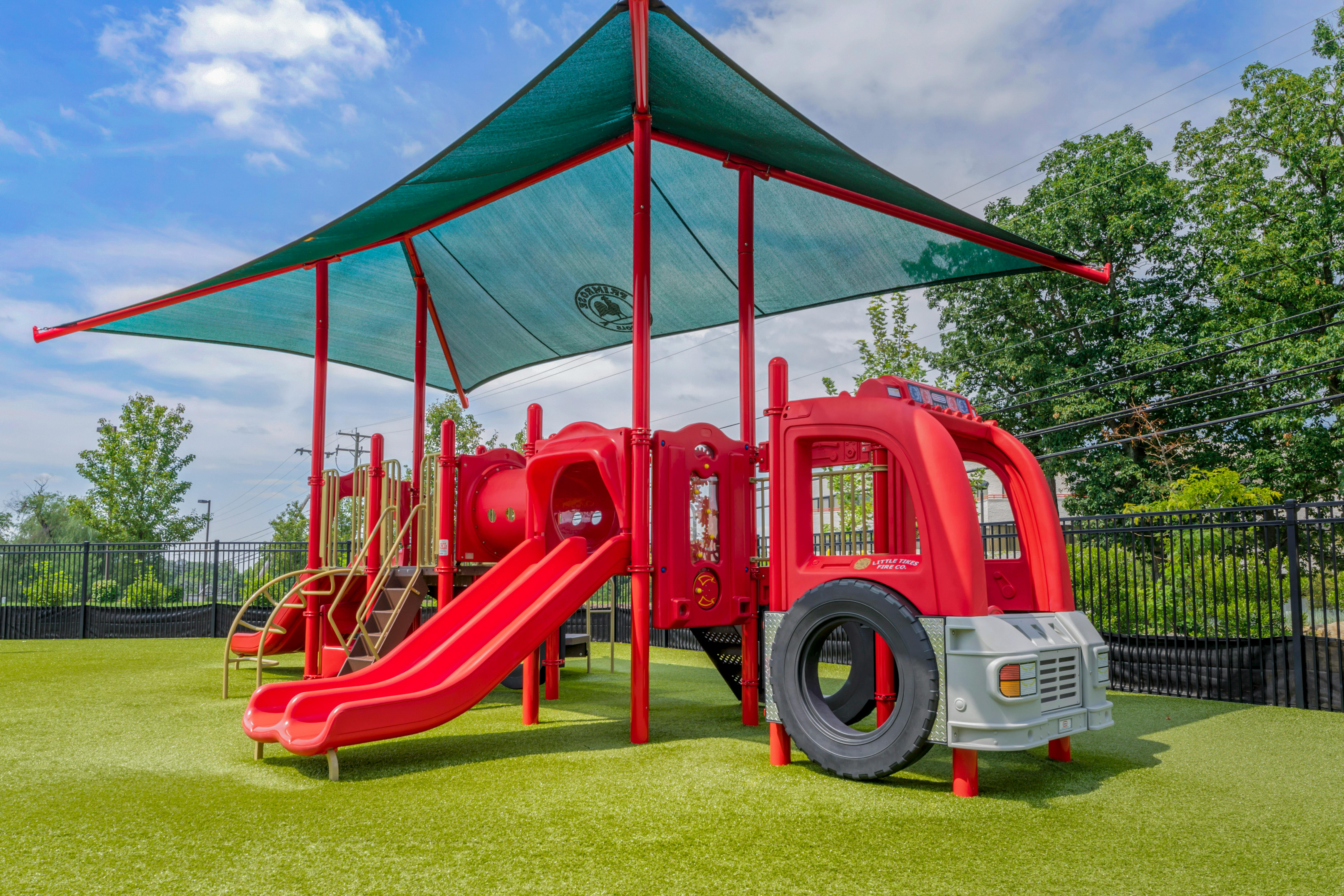 Red playground structure with slides and a fire truck front under a green canopy