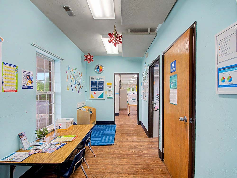 Hallway with light blue walls, two windows, a wooden table with chairs, and doors