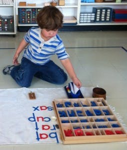 Child kneeling on floor, arranging letter tiles on a mat