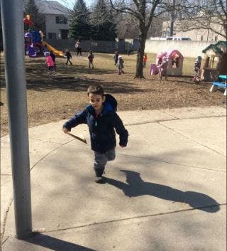 Child running with a stick on a paved surface in a playground