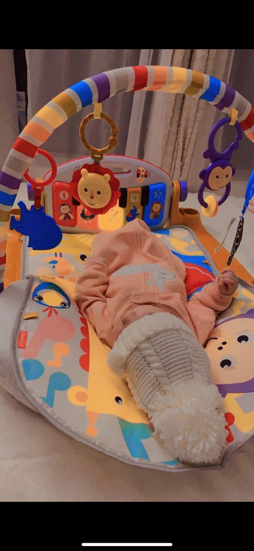 A child lying on a colorful activity mat with hanging toys