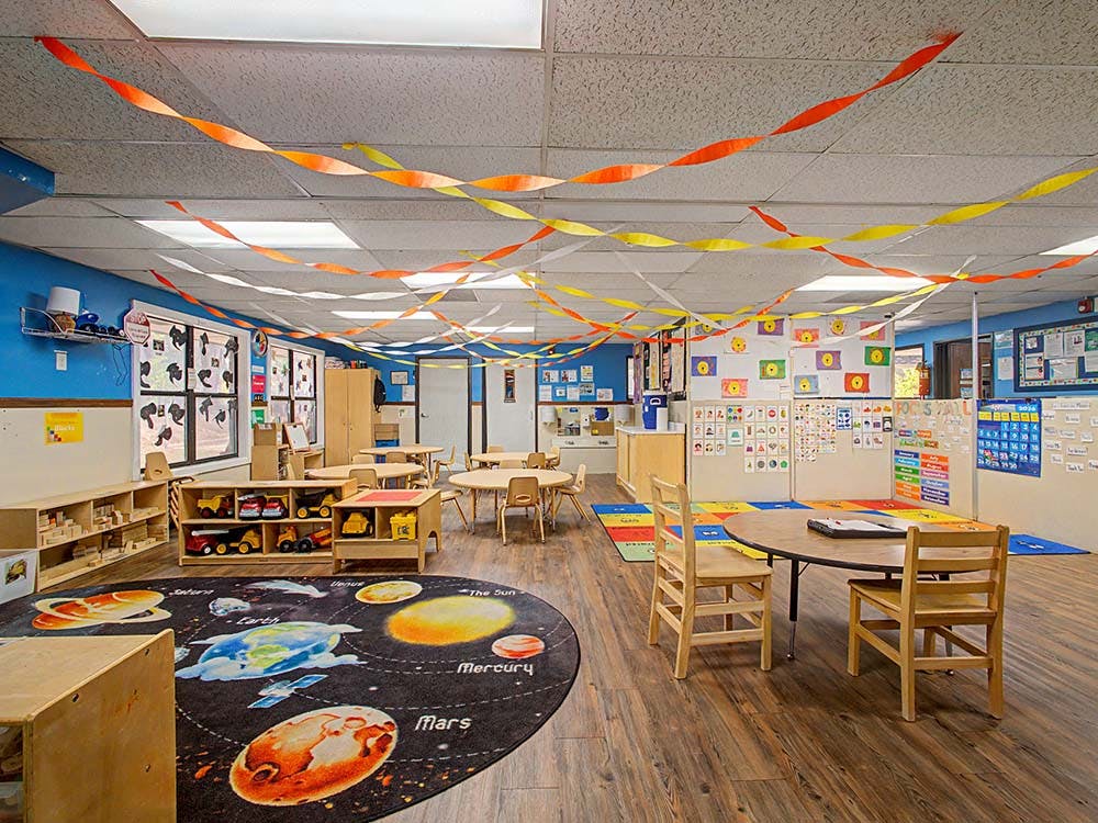 An empty classroom with colorful decorations, tables, and a space-themed rug