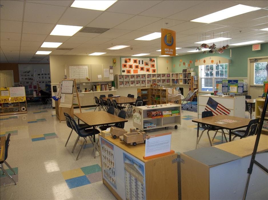 An empty classroom with tables, chairs, bookshelves, and various learning materials