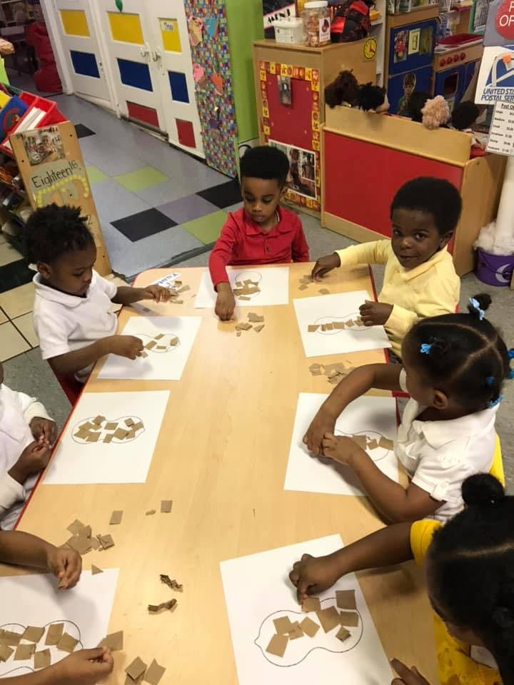 Children at a table working on craft projects with small paper squares