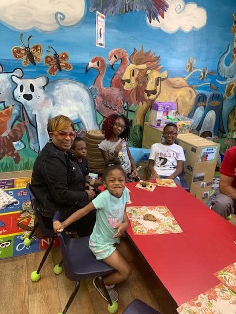 Adult and children sitting at a red table in a room with animal murals