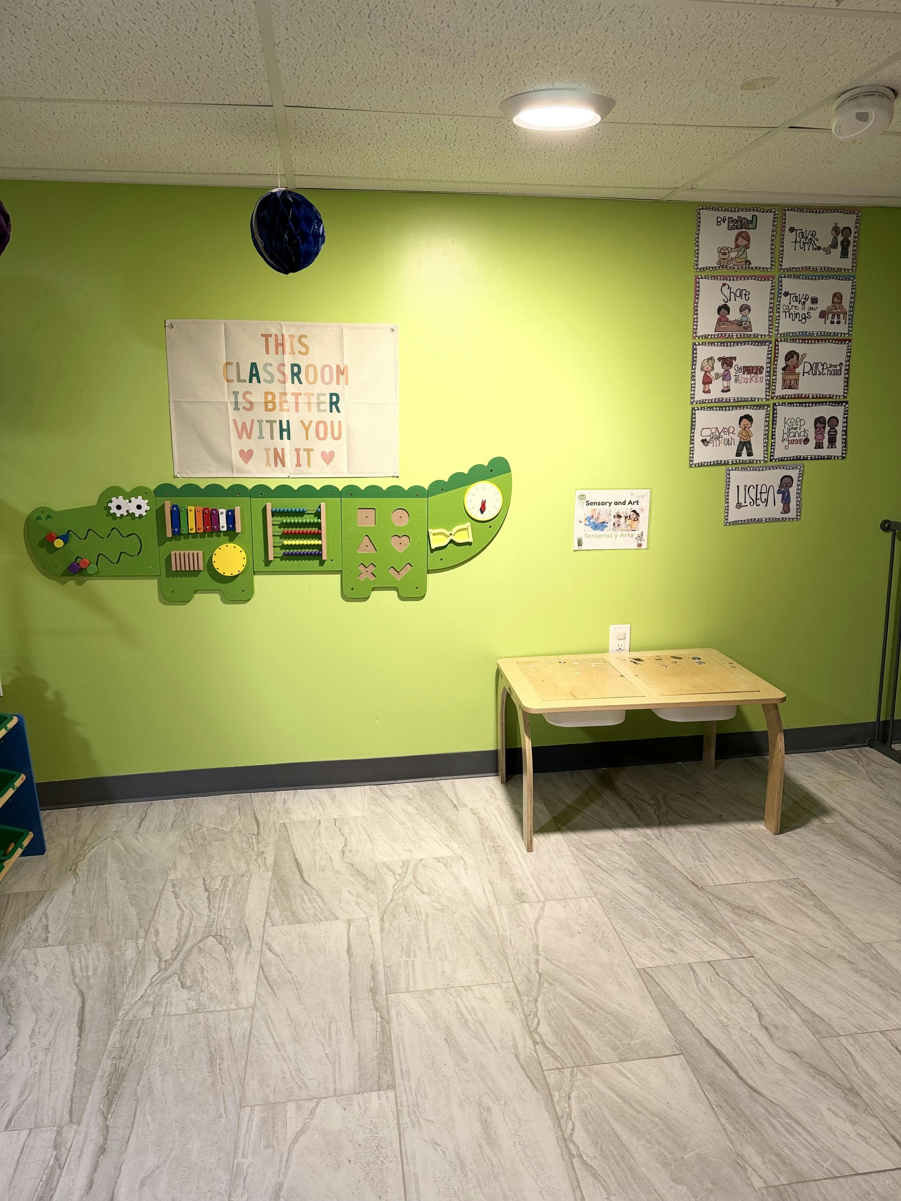 Classroom with a green wall, alligator-shaped activity board, and small wooden table