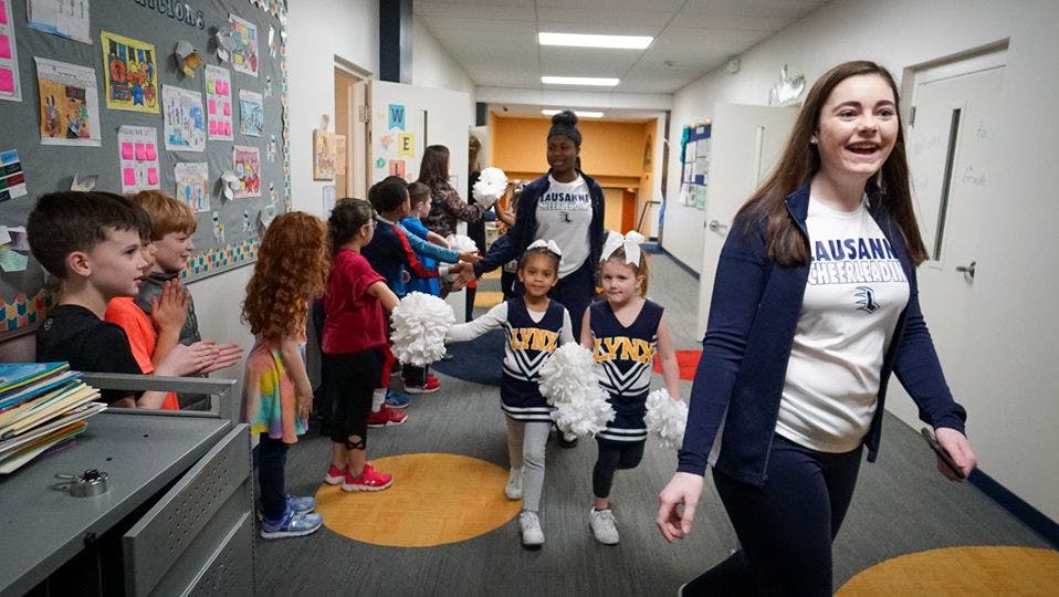 Adult and children walking in a school hallway, some children in cheerleading outfits