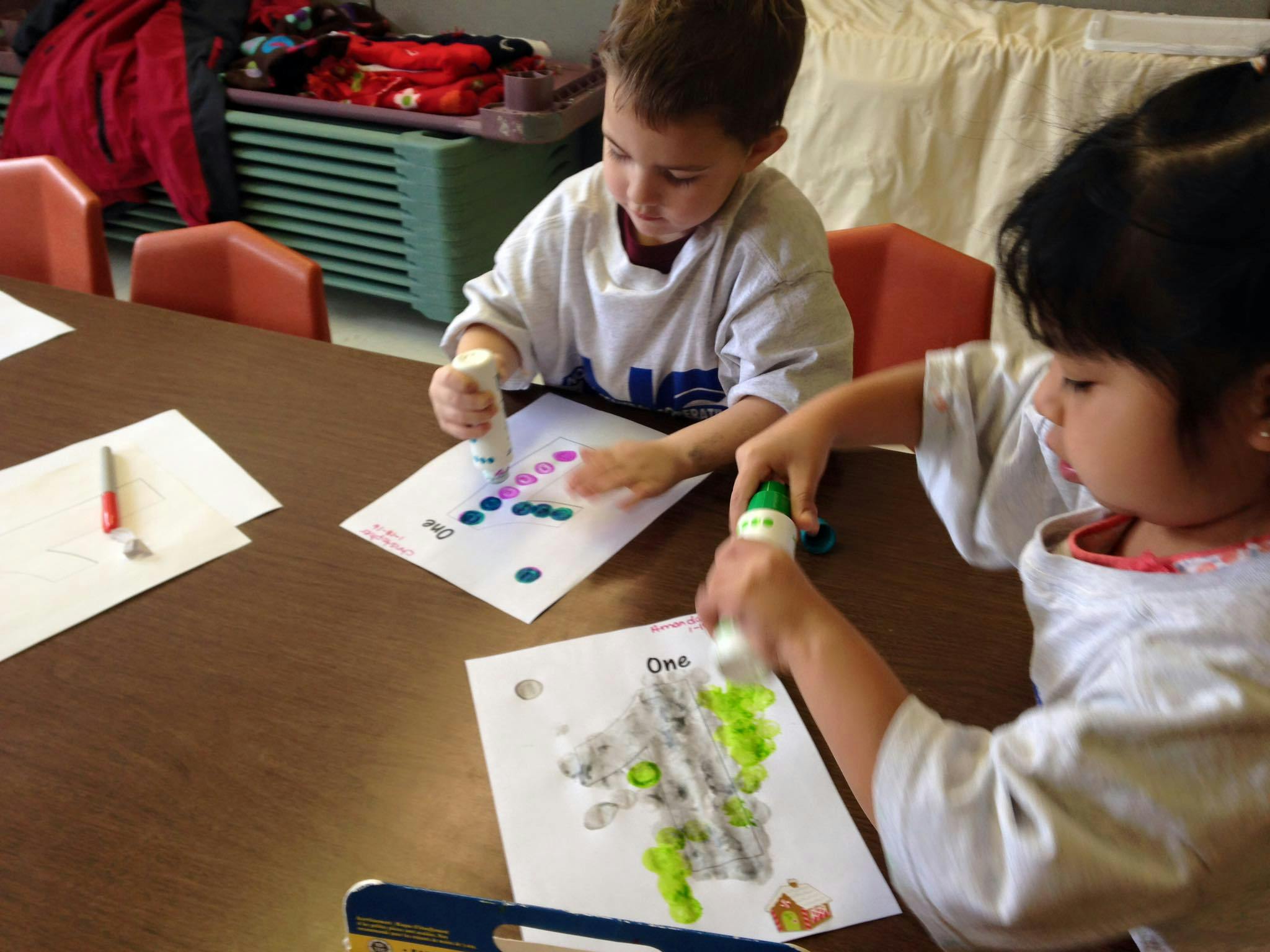 Two children making art with paint daubers at a table