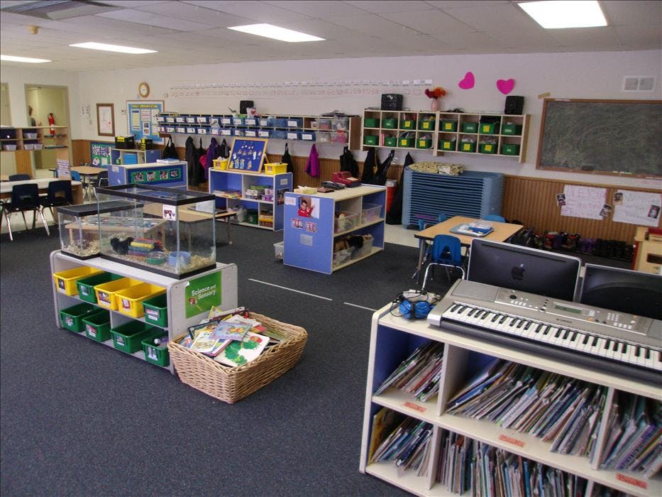 An empty classroom with desks, shelves of books and learning materials, and animal enclosures