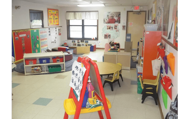 An empty children's classroom with small tables, chairs, and activity areas