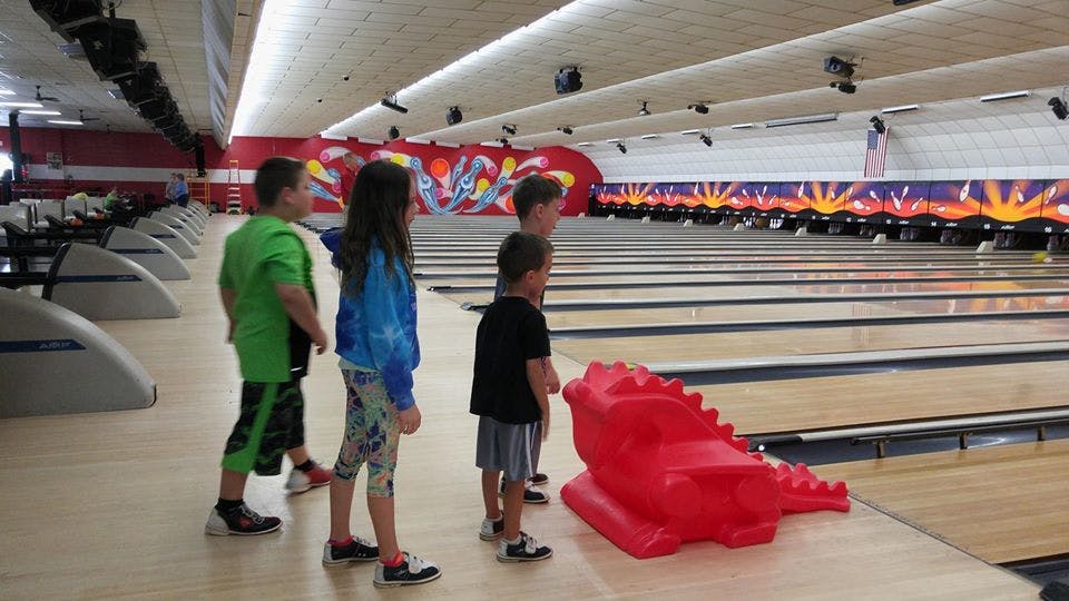 Children bowling with a red dinosaur-shaped ramp