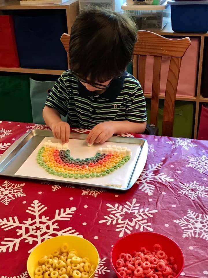 Child making a rainbow shape with colorful cereal pieces on a tray