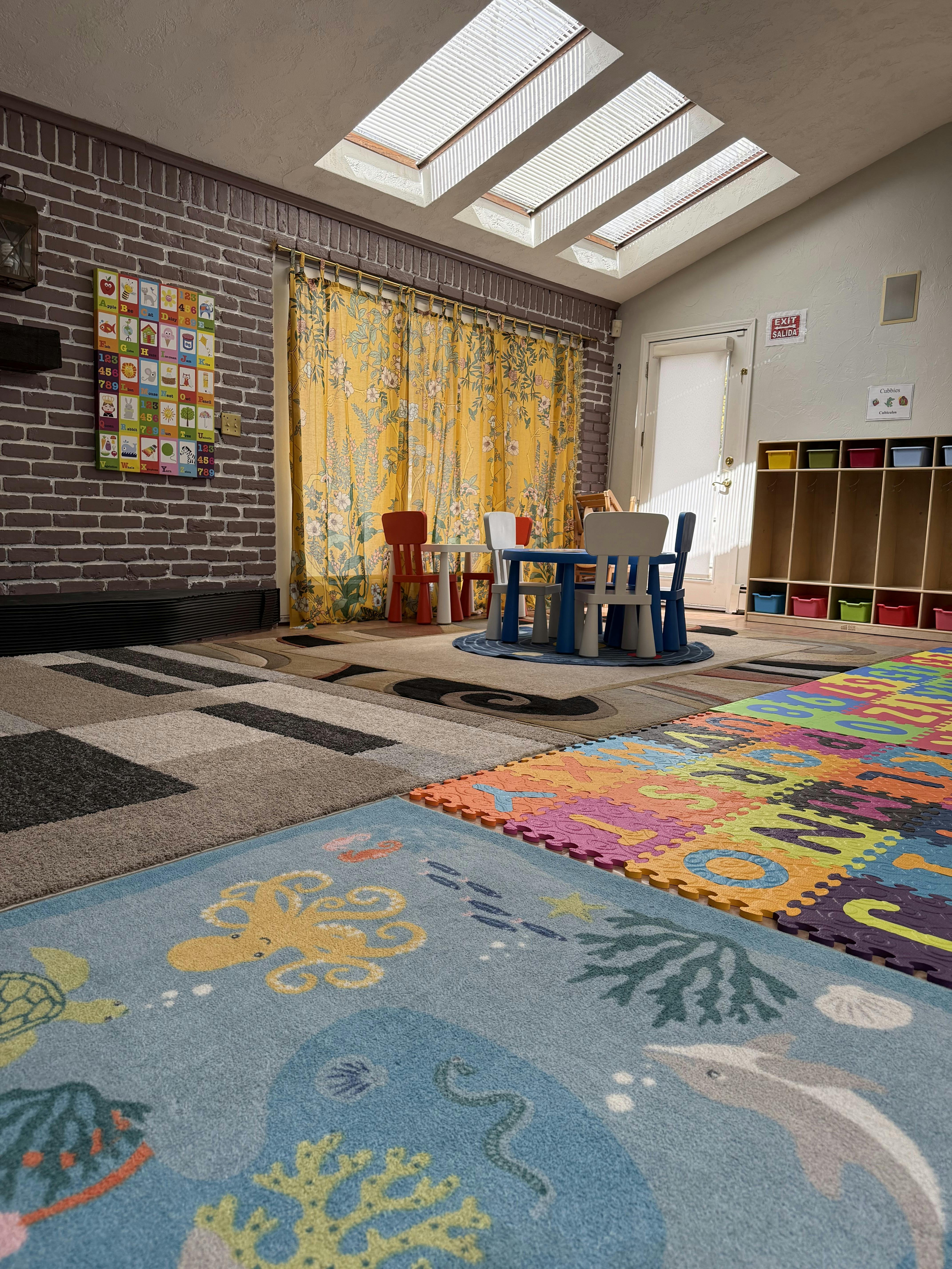 Playroom with small tables and chairs, colorful rugs, and skylights