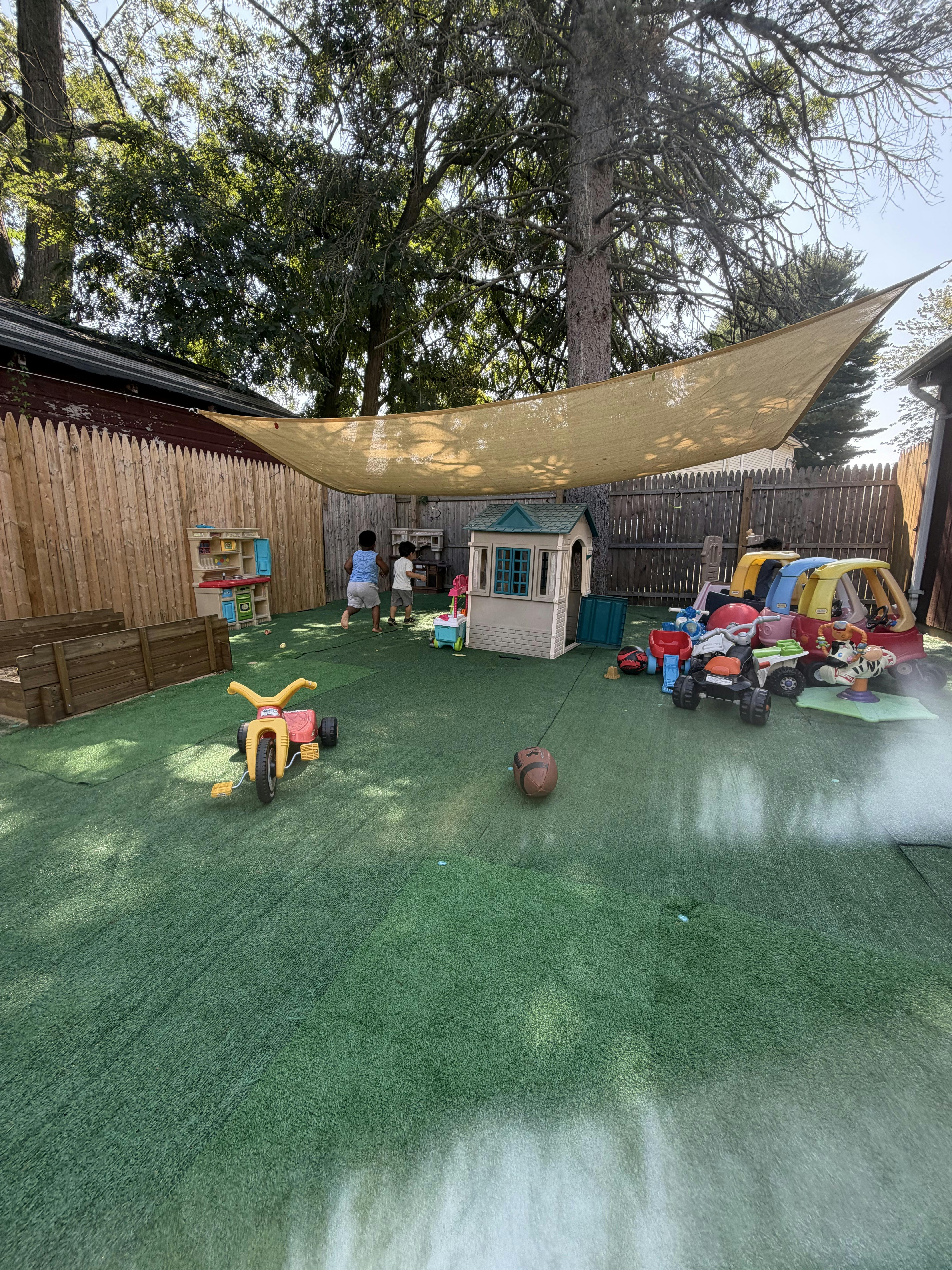 Children playing in a backyard with toys under a shade sail