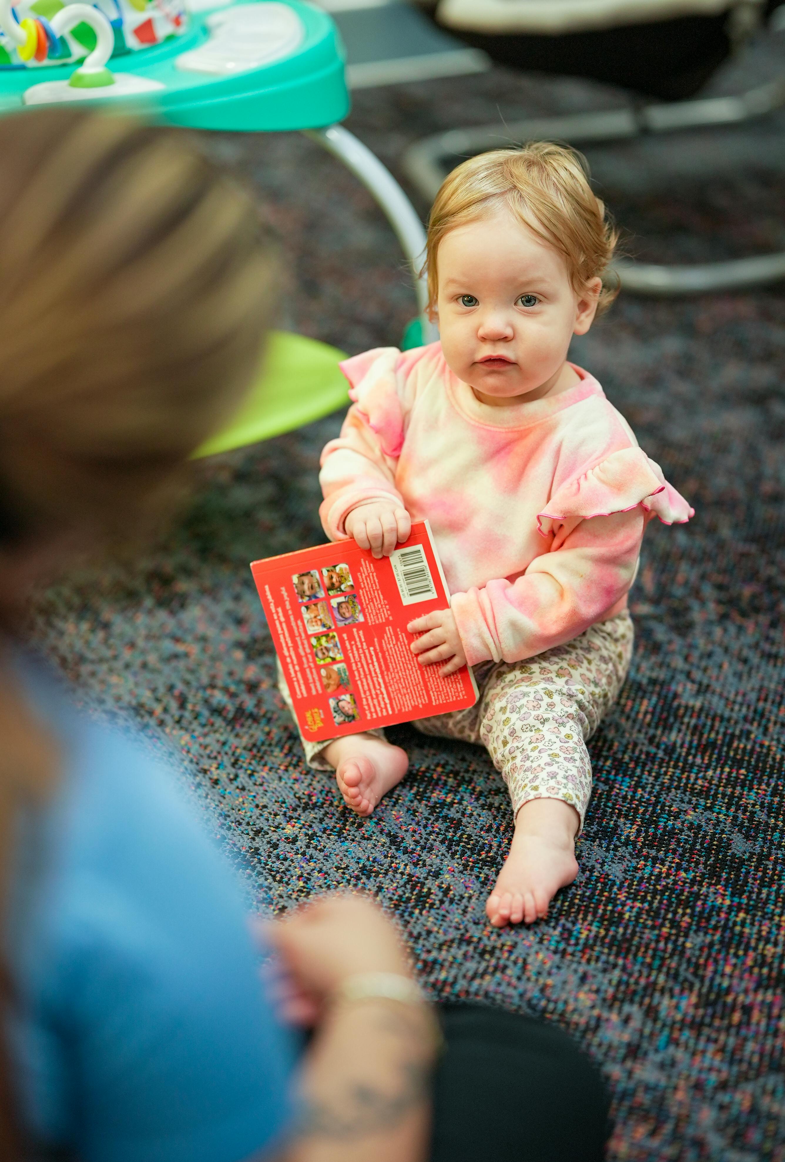 Child sitting on floor holding a red book