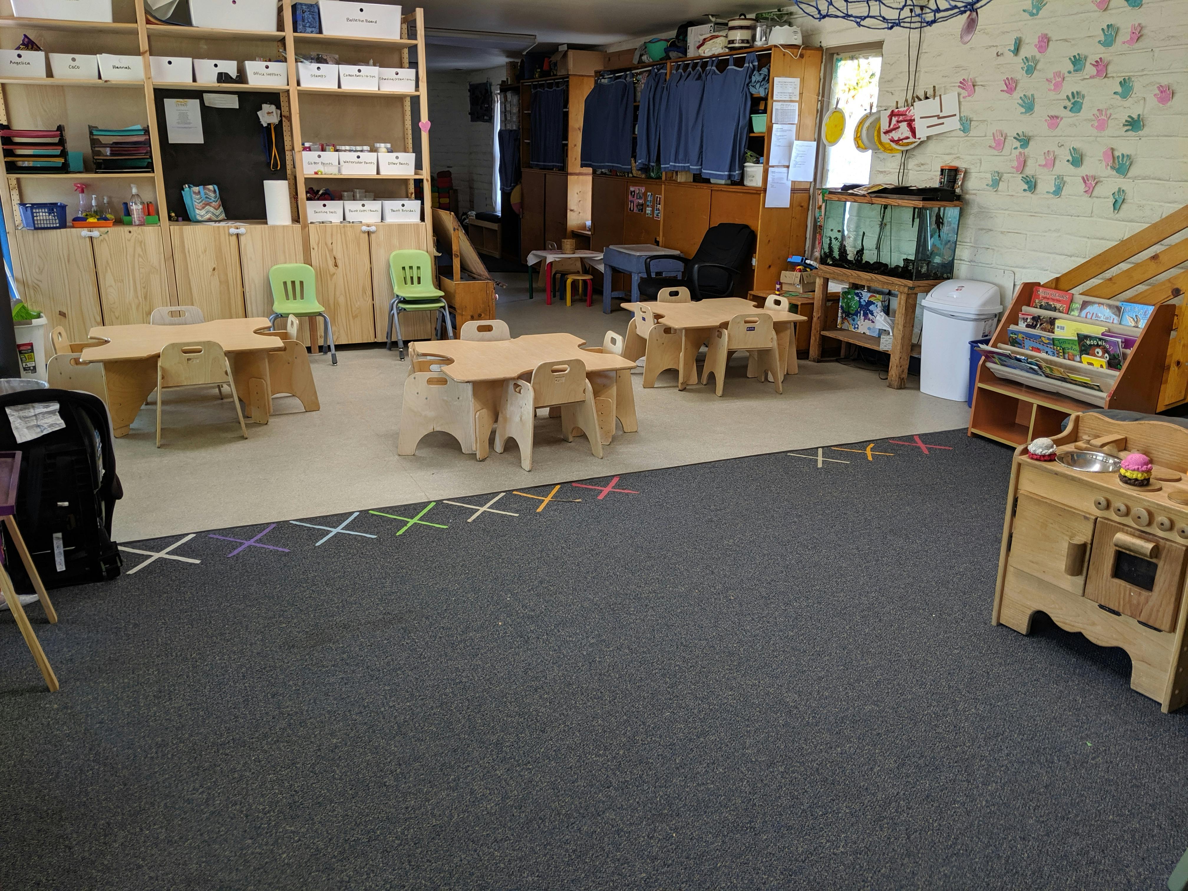 Classroom with small tables and chairs, shelves, and play kitchen