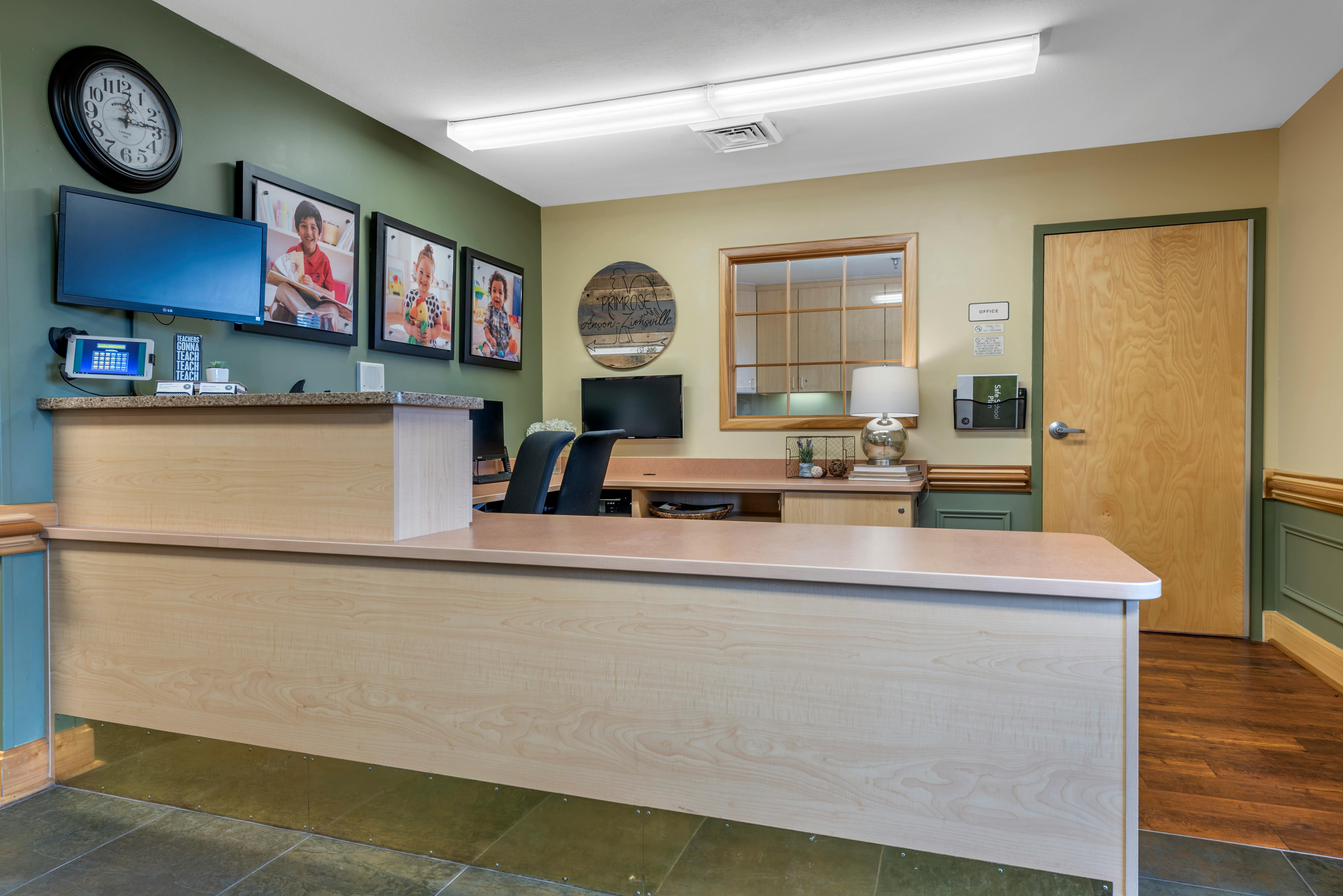 Reception desk with three framed photos of children and a wall-mounted clock