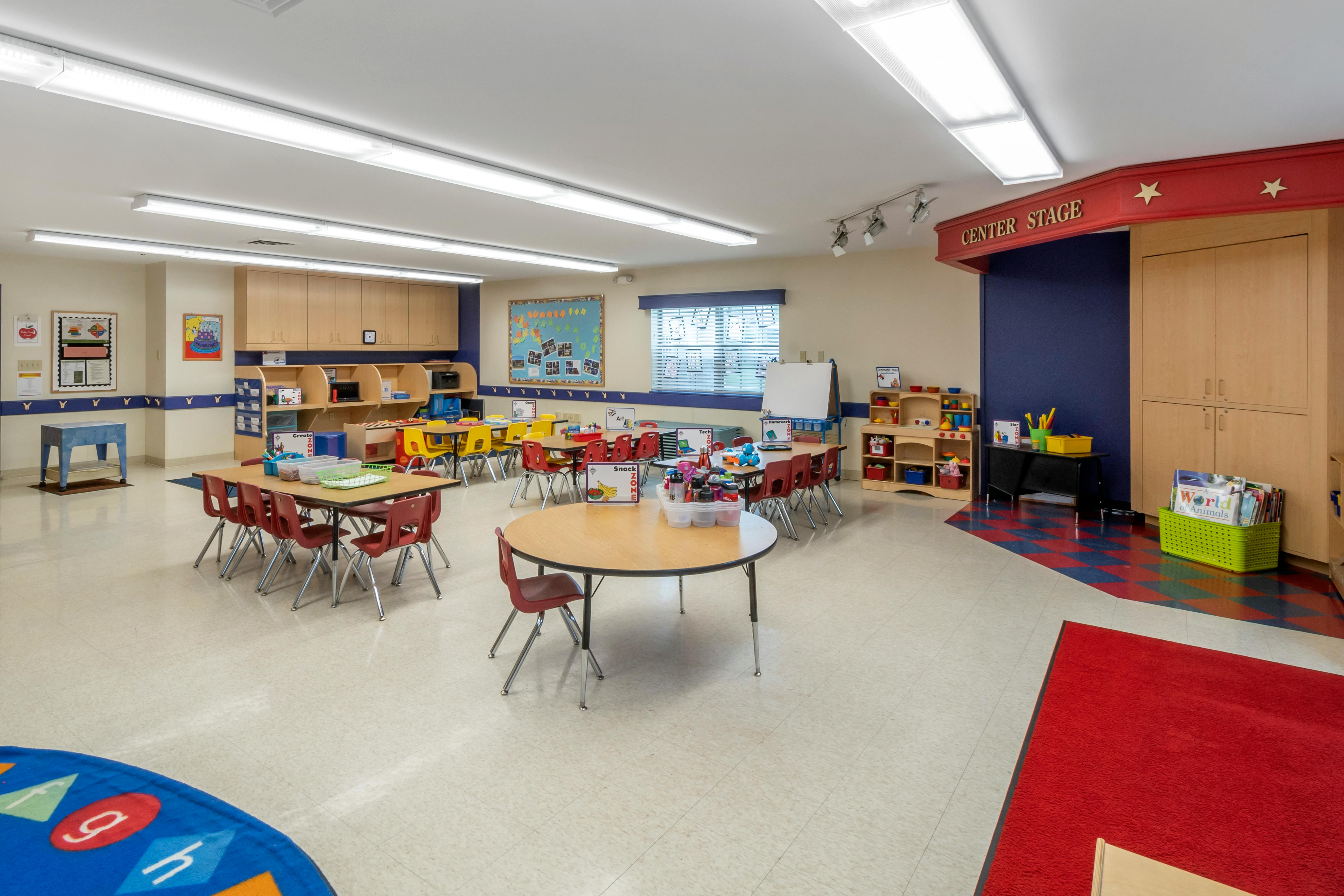 Empty classroom with small tables and chairs, bright lighting, and various learning stations