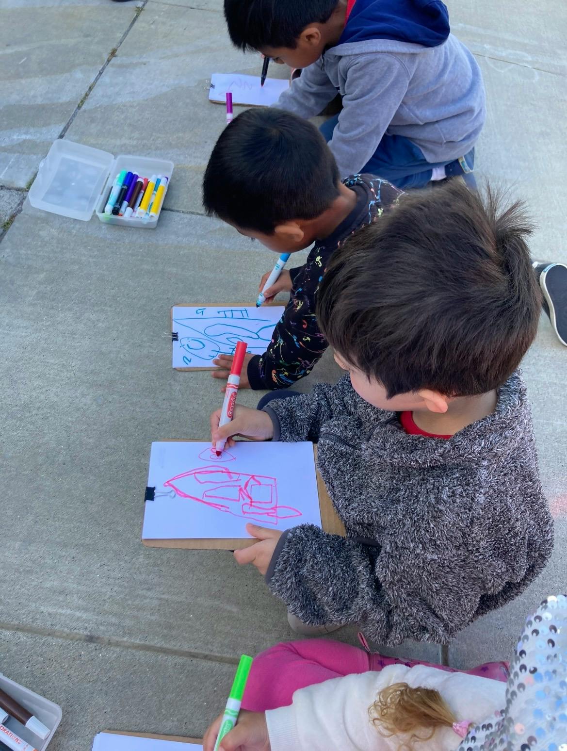 Children drawing on clipboards on the ground