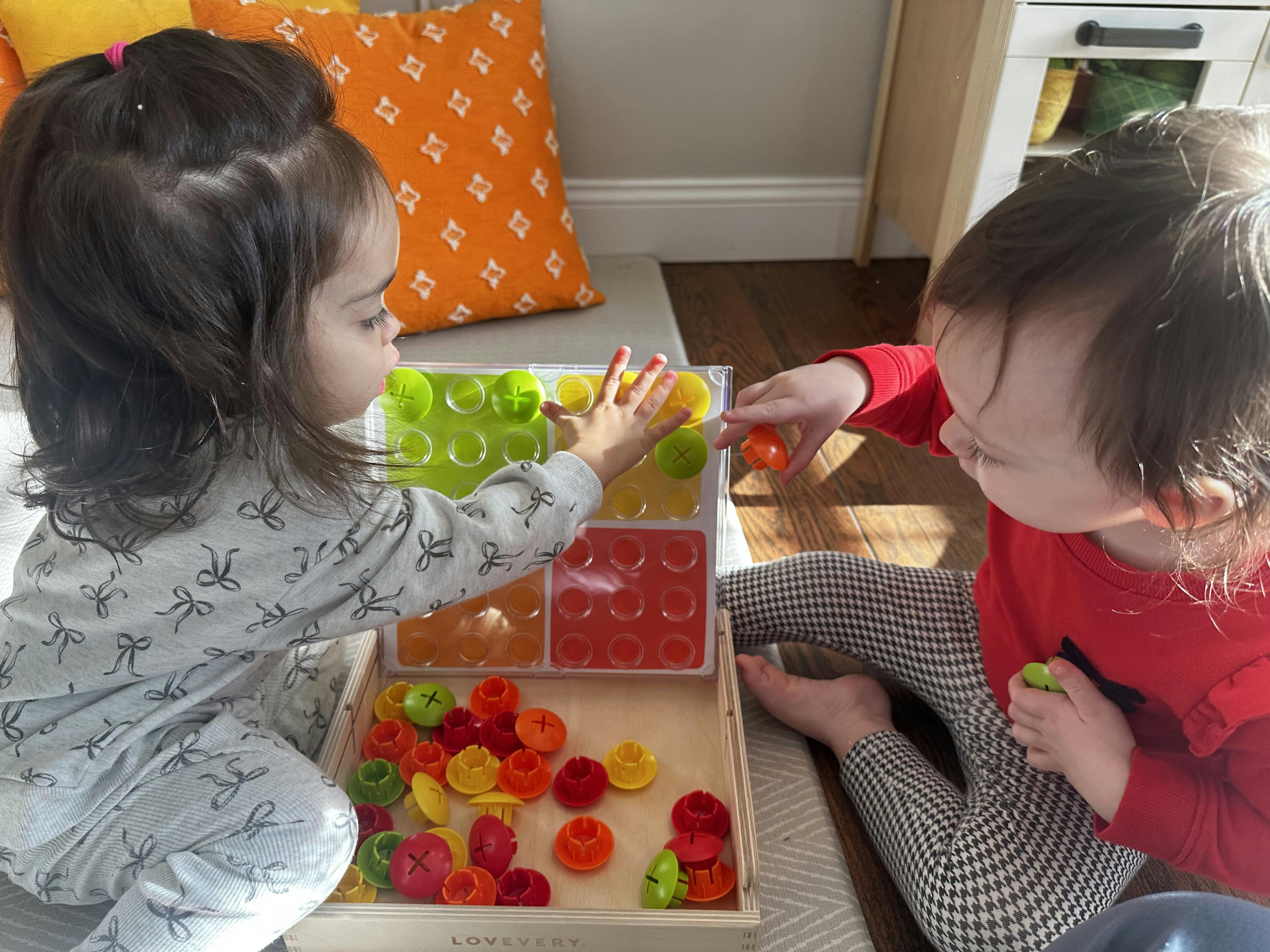 Two young children playing with a colorful pegboard and board toy
