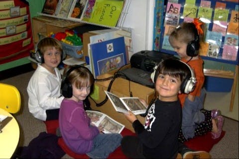 Four children wearing headphones and looking at books