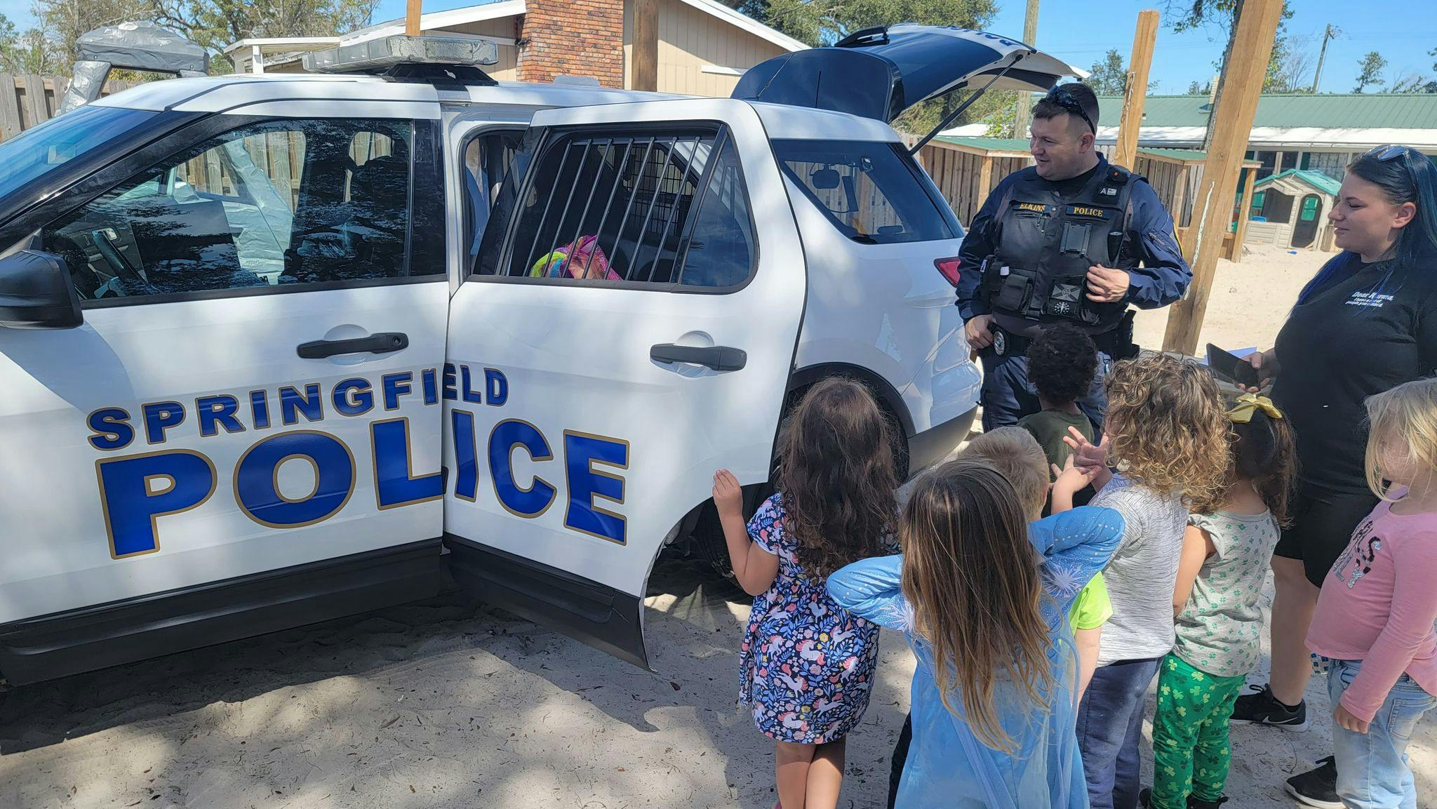 Police officer and another adult with children gathered around a police vehicle
