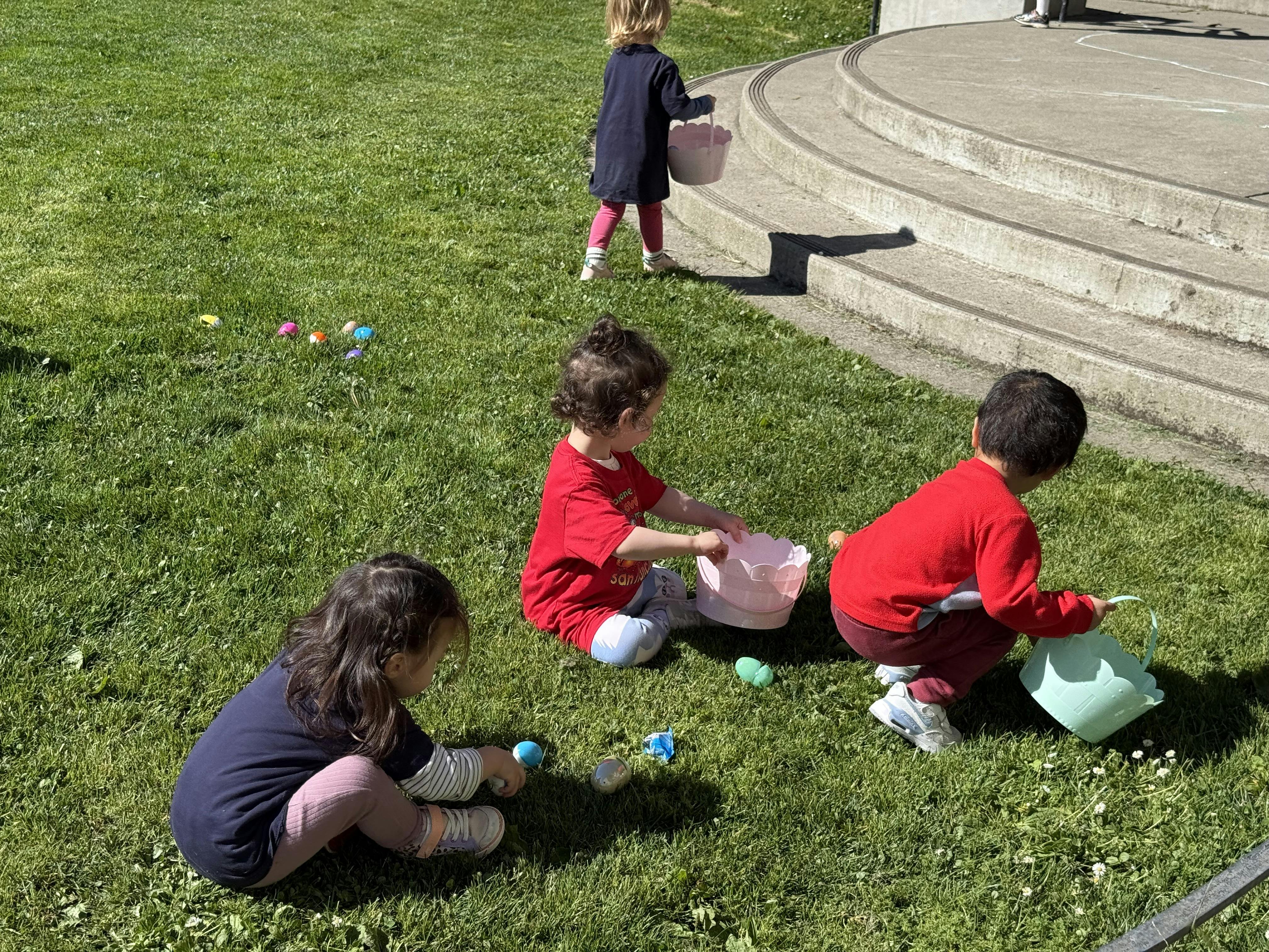 Children collecting eggs in baskets on a grassy lawn