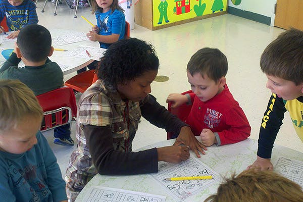 Adult and children drawing at a table in a classroom
