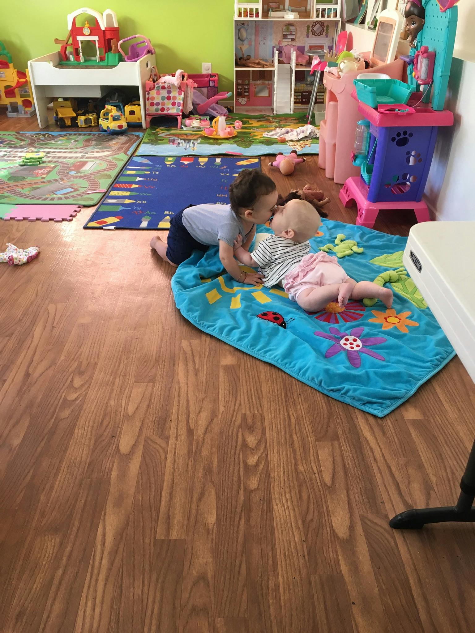 Child leaning over another child on a blue blanket in a playroom